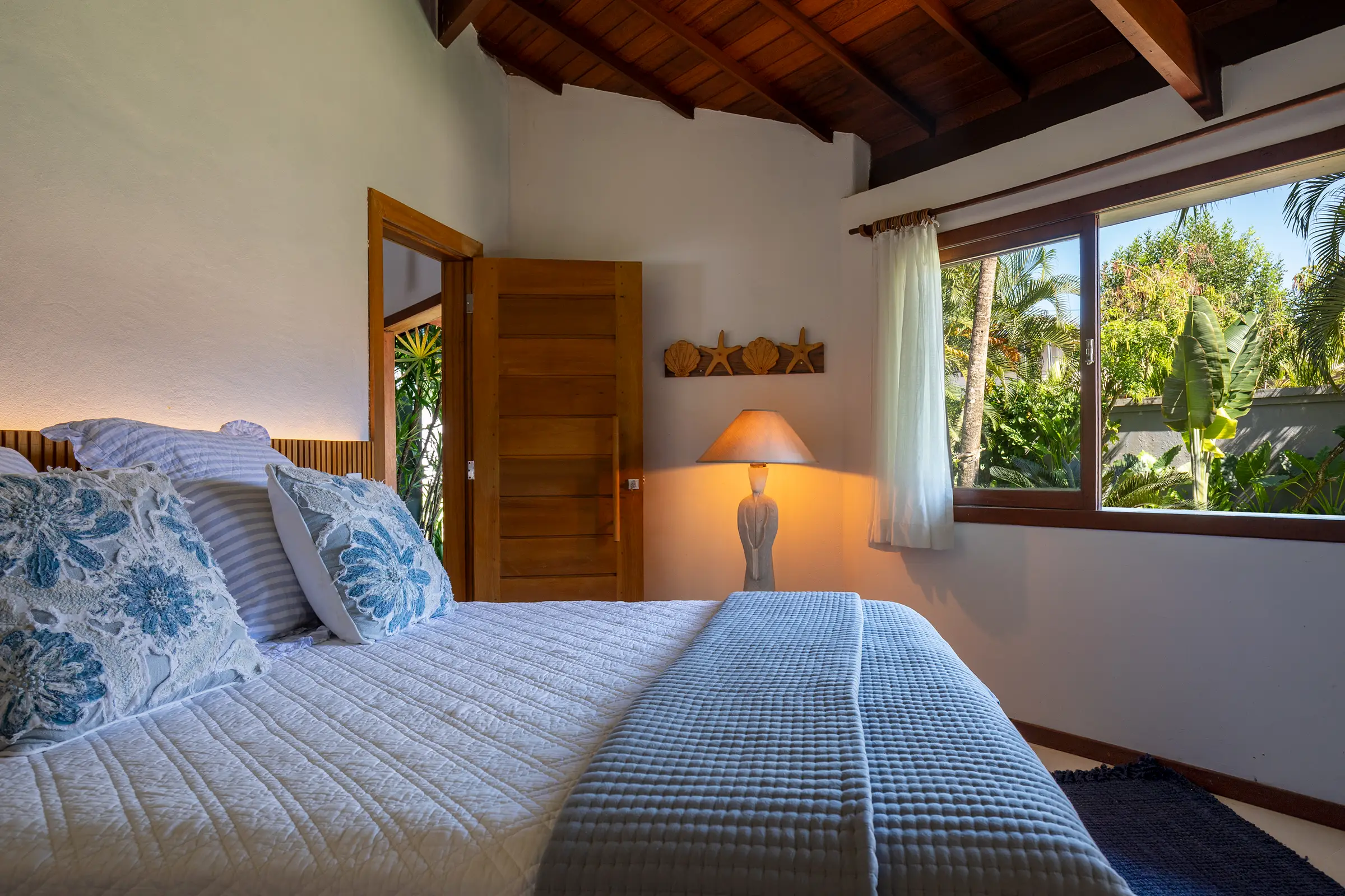 Quarto com roupa de cama azul e branca e janela para o jardim