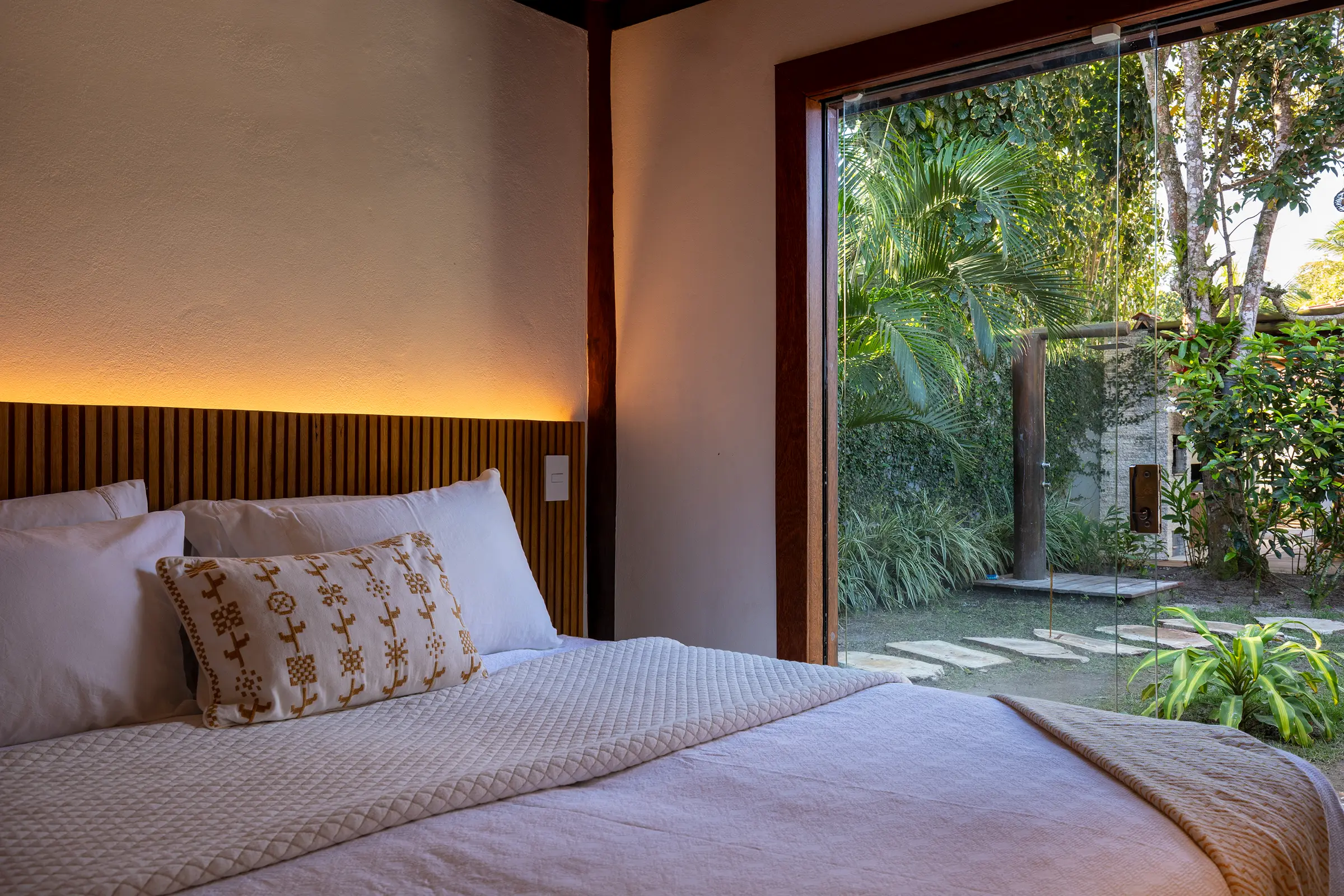 Cama com cabeceira de ripas de madeira e vista para o jardim