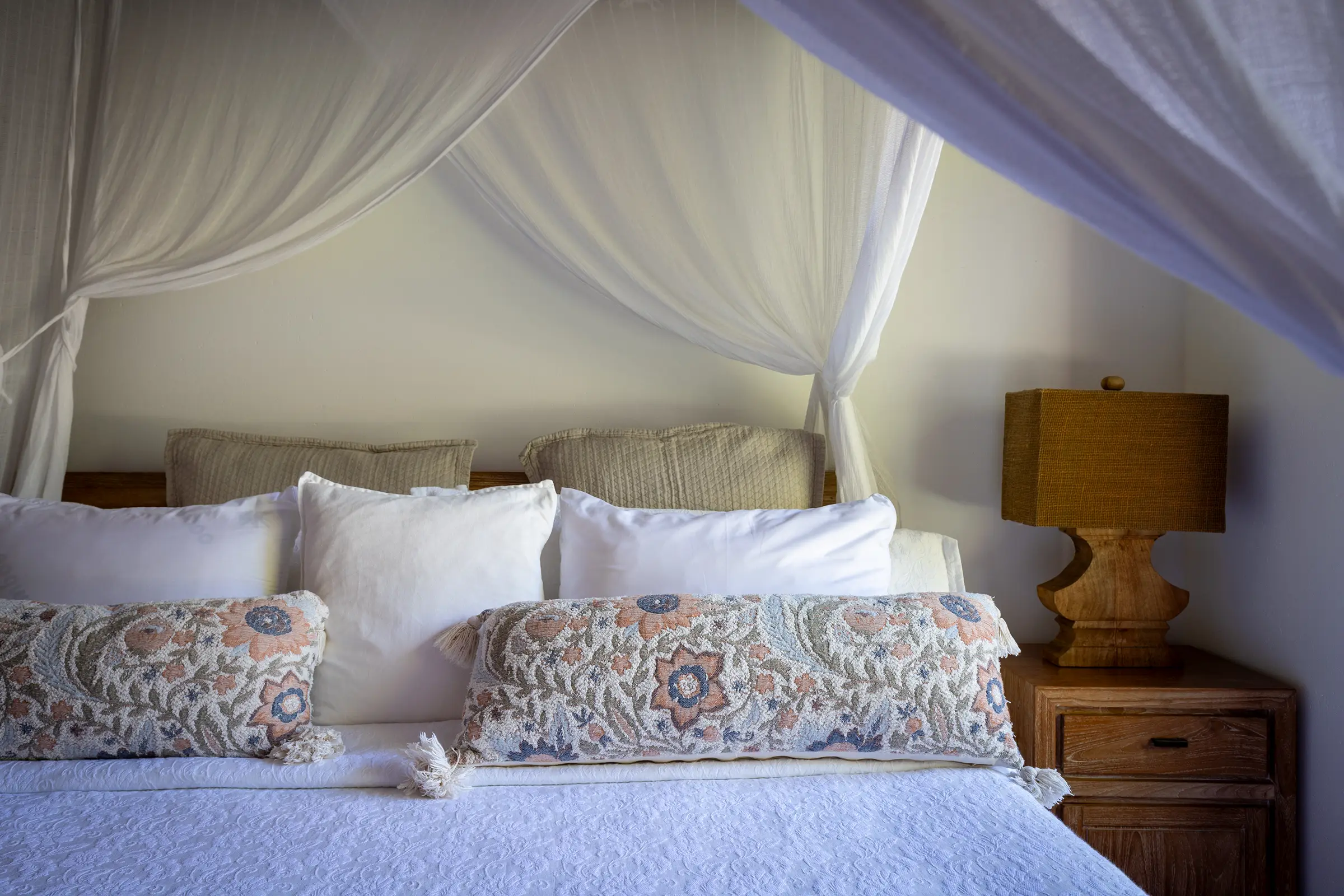 Detalhe da cama com almofadas e abajur de madeira