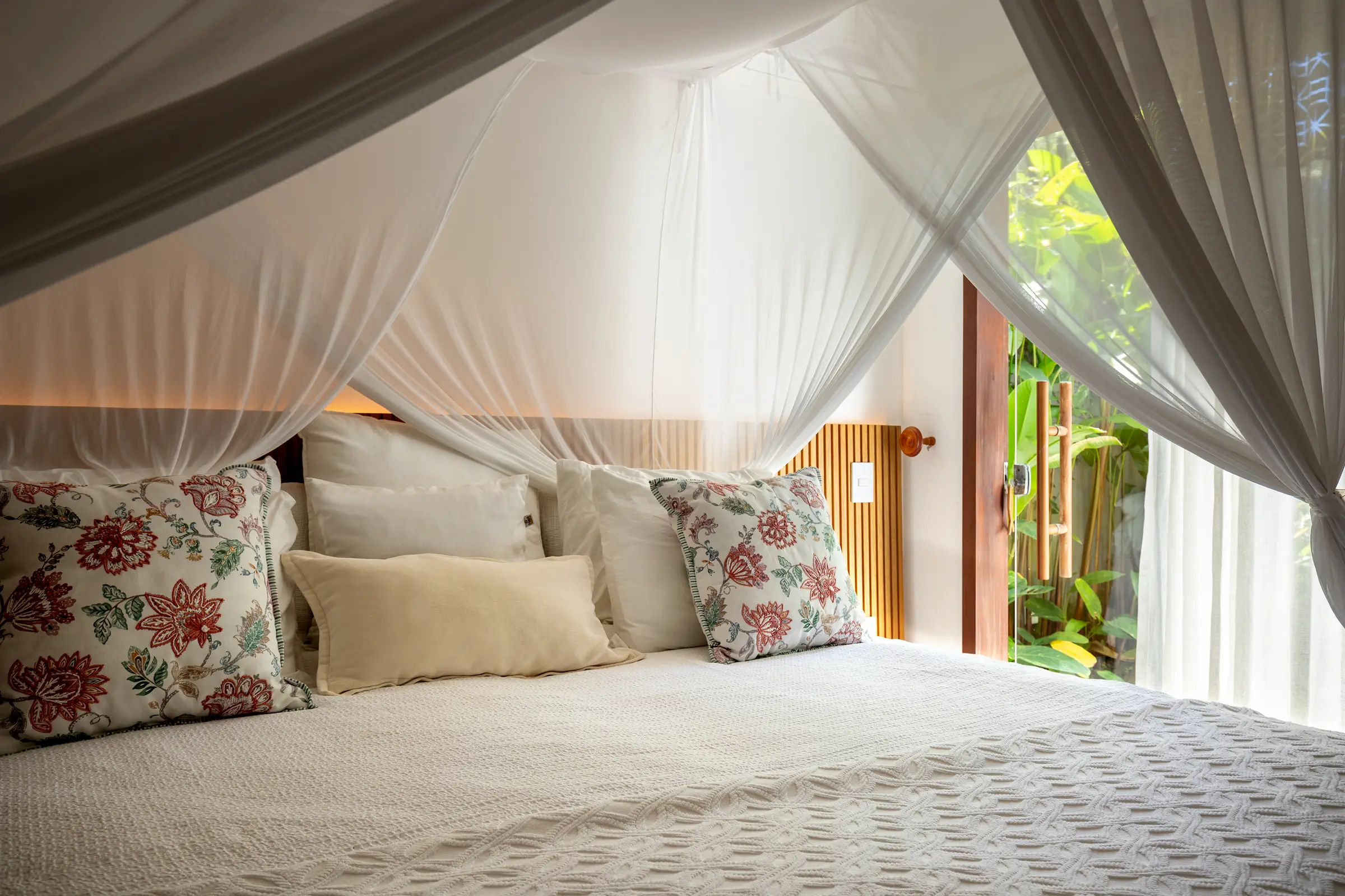 Cama com travesseiros estampados e mosquiteiro, luz de fim de tarde