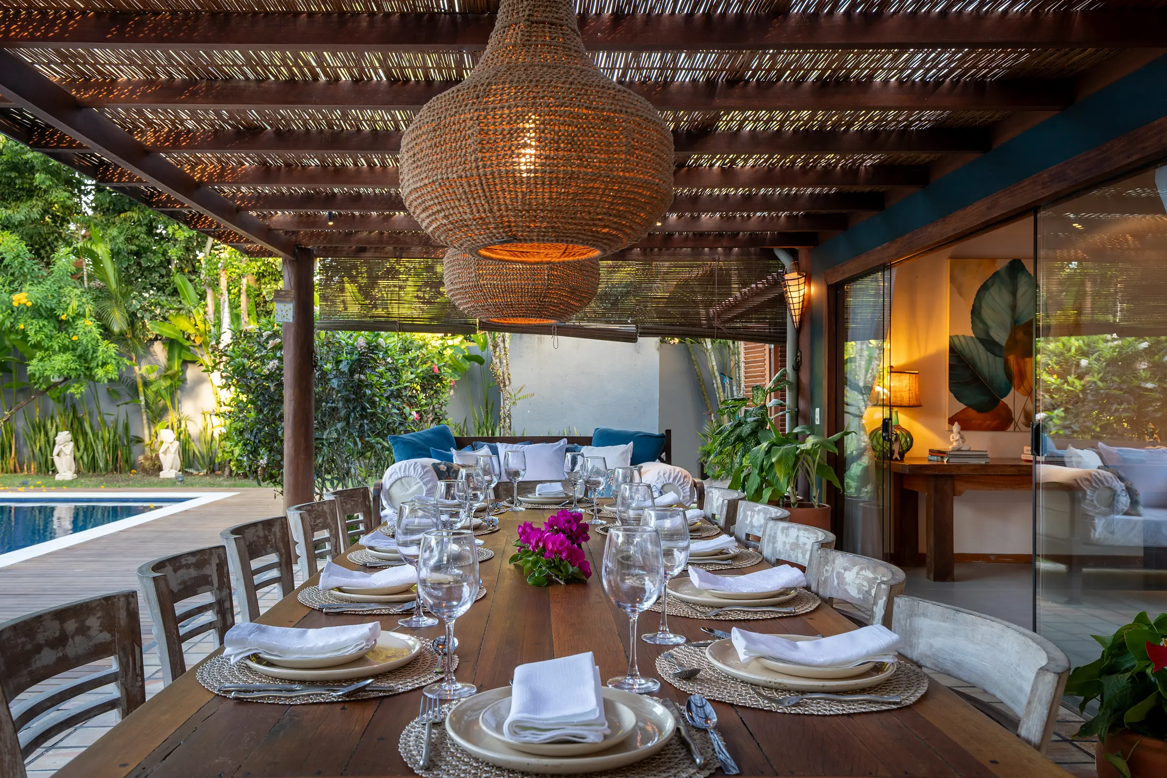 Mesa longa posta para um jantar em grupo, com luminárias de palha e jardim