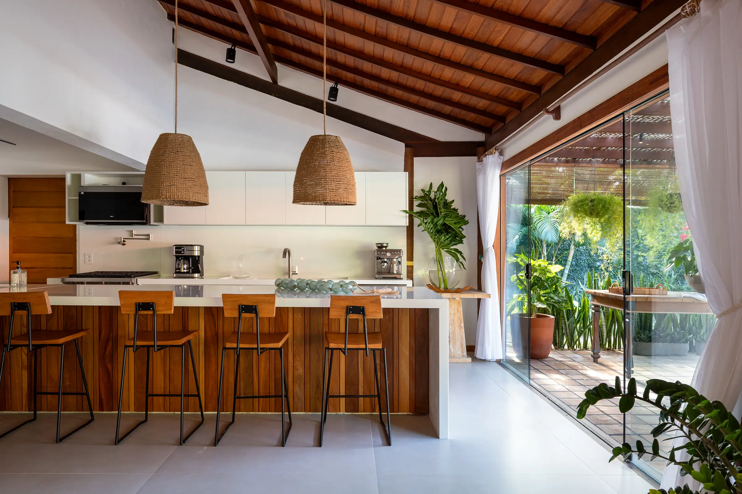 Cozinha com bancada de madeira, banquetas e janela para o jardim