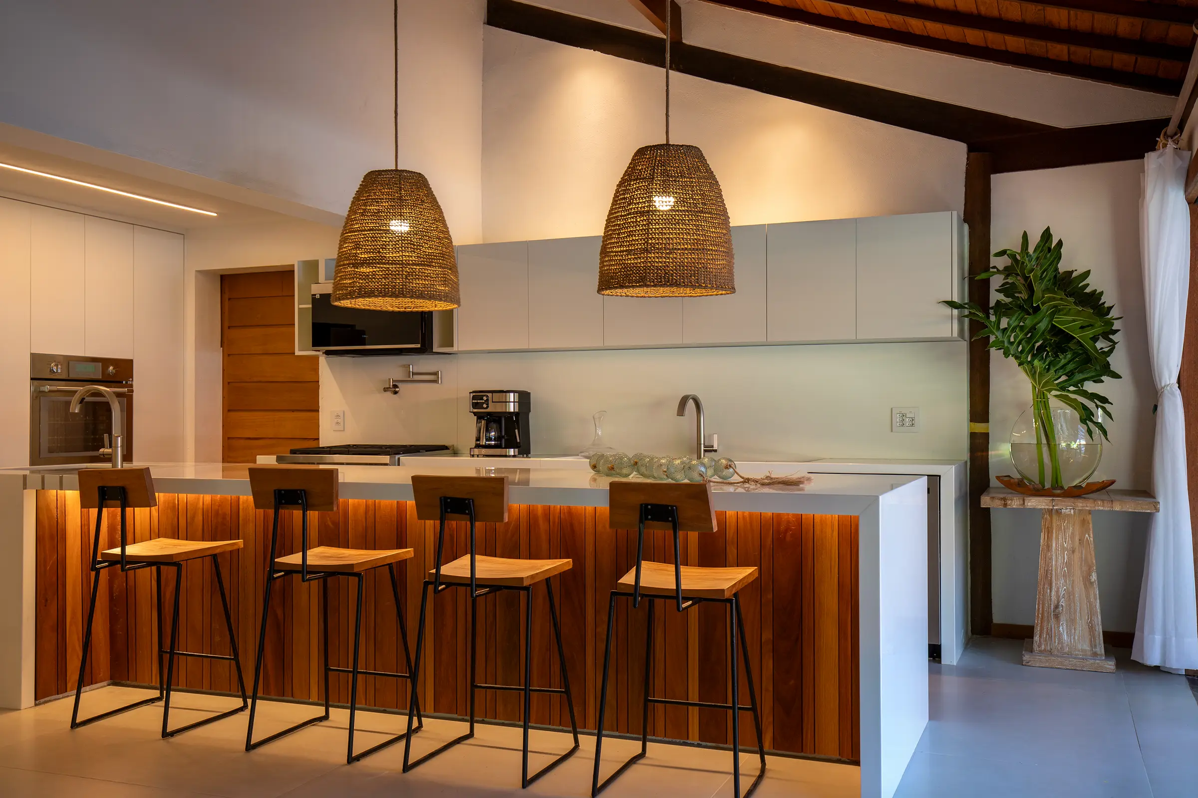 Ilha da cozinha com banquetas e luminárias de palha