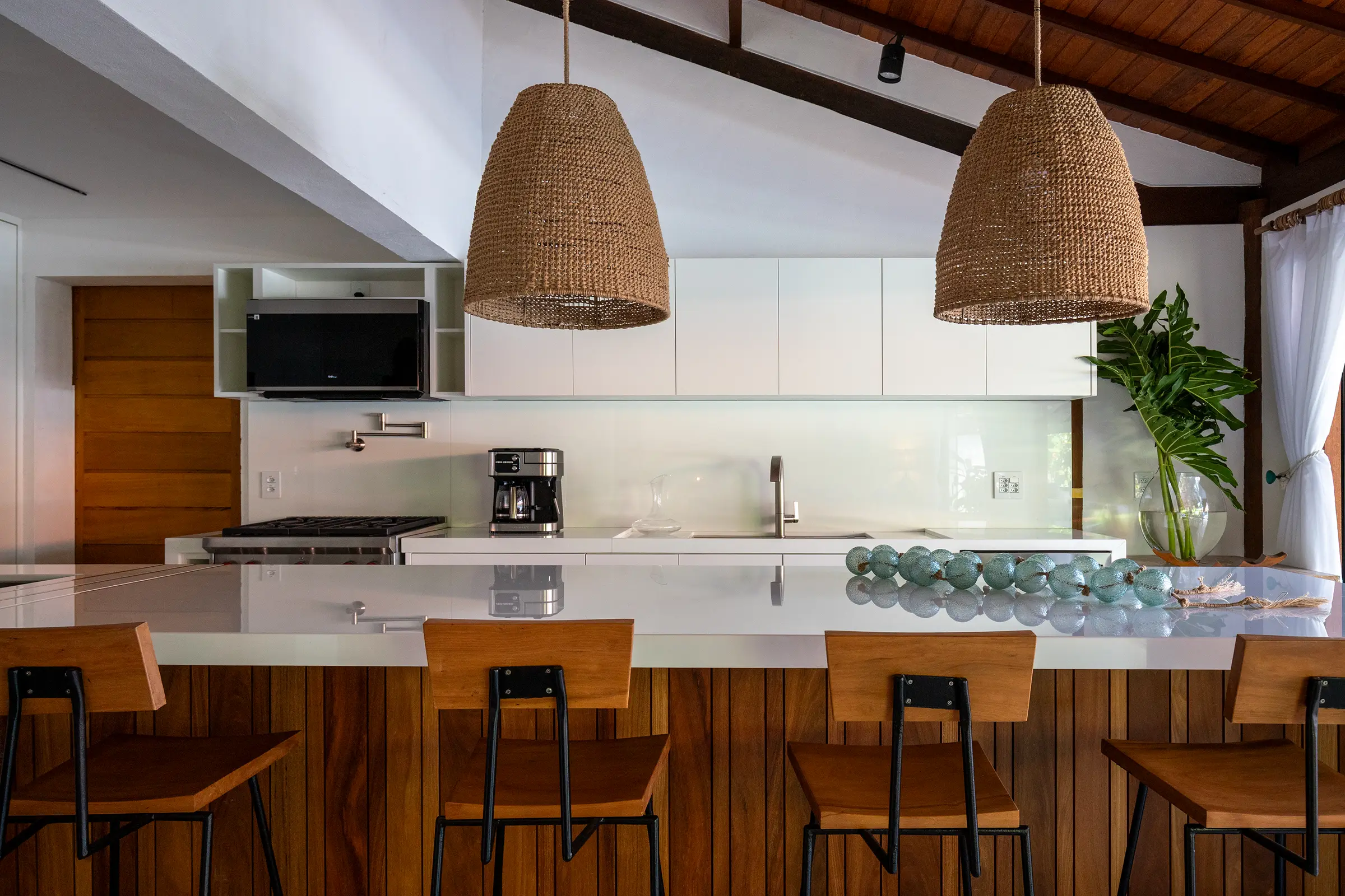 Ilha da cozinha com luminárias de palha e banquetas de madeira