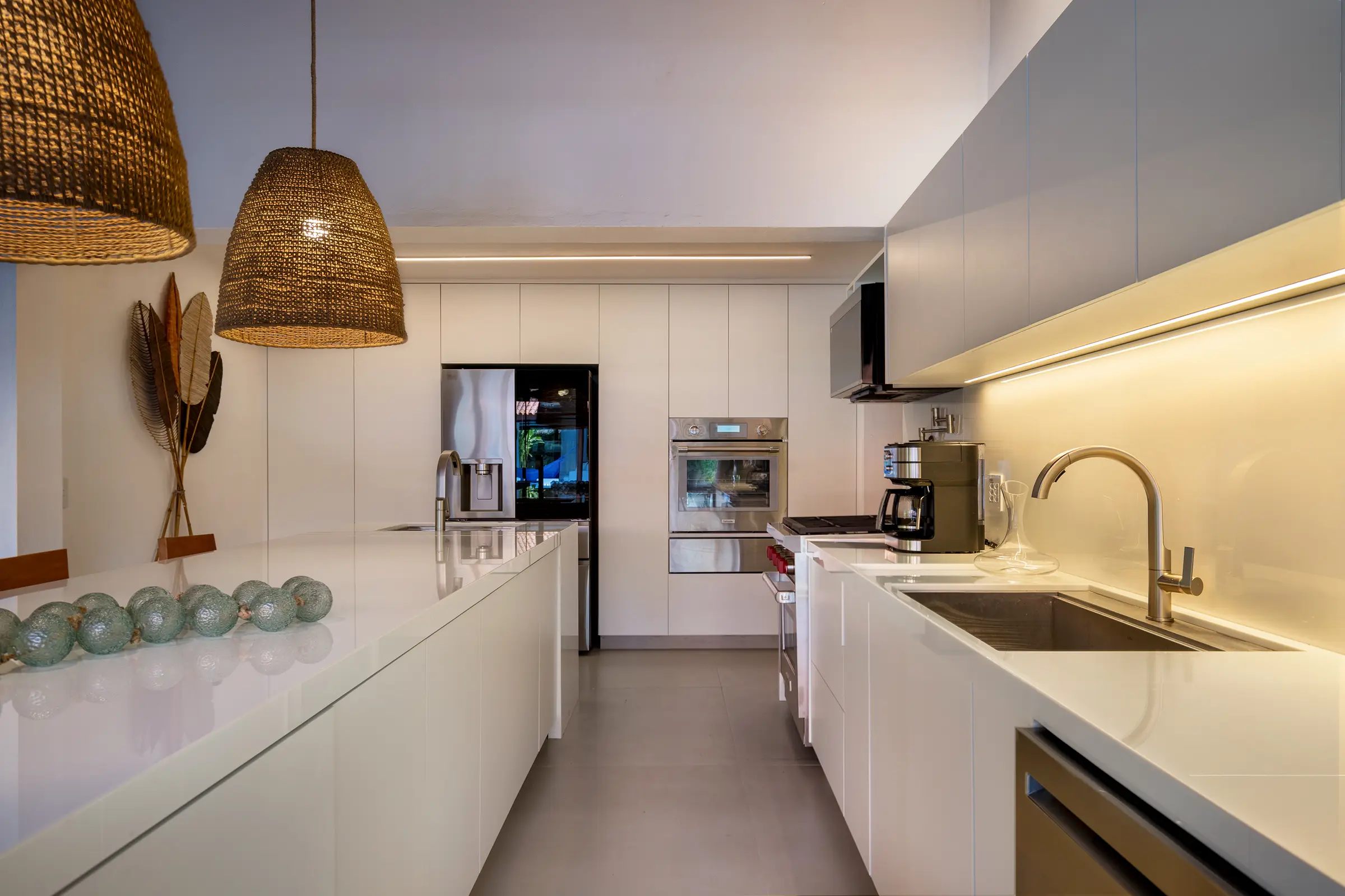 Cozinha branca com bancada comprida e luminária de palha