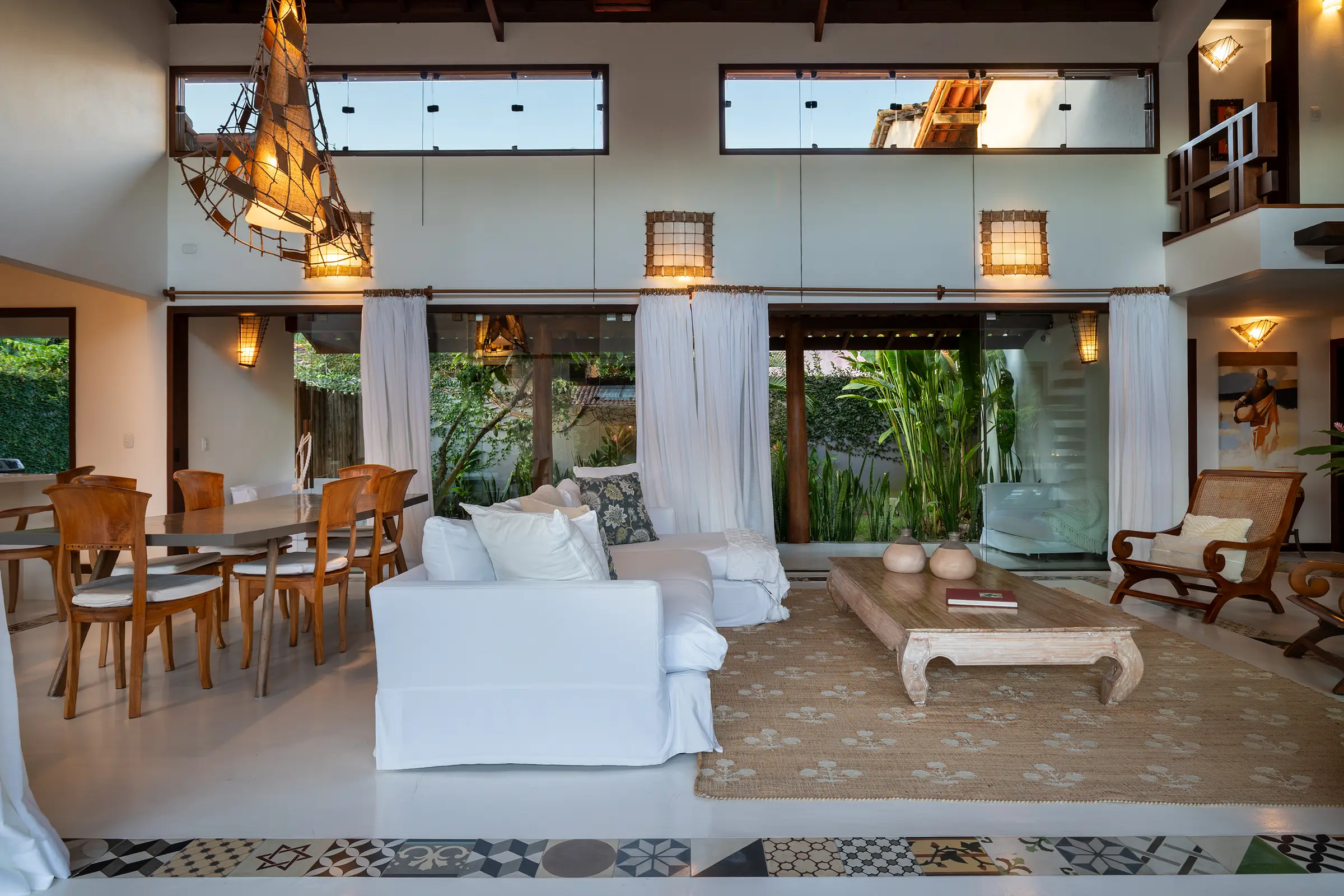 Sala ampla com sofá branco, mesa de jantar de madeira e cortinas brancas