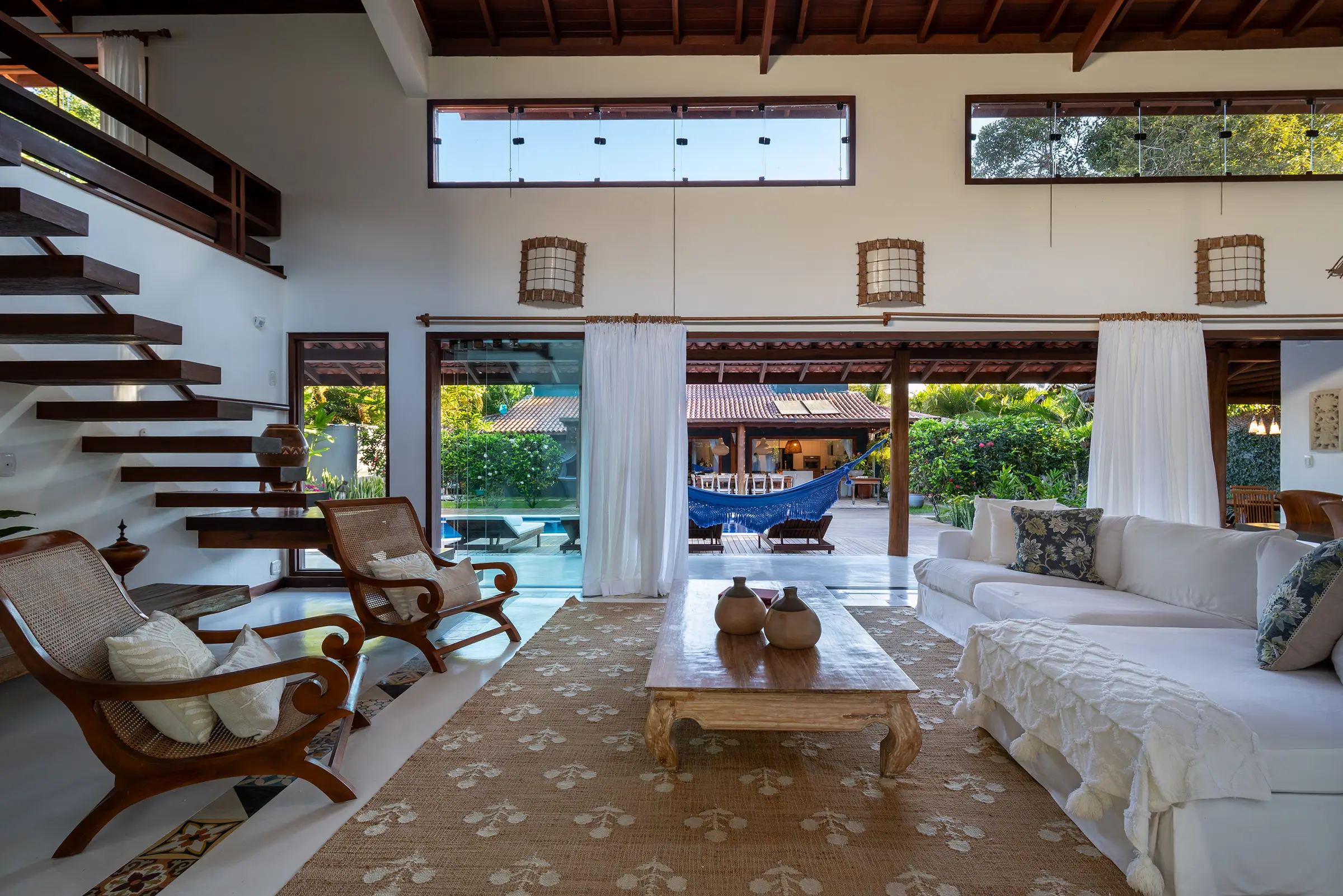 Sofás brancos e poltronas de palhinha com a piscina ao fundo