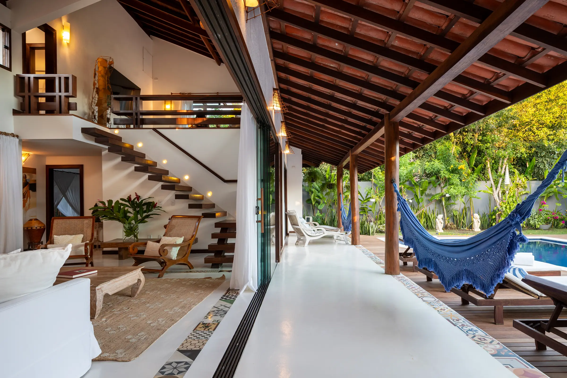 Sala com escada de madeira e portas de vidro abertas para a varanda e a rede azul