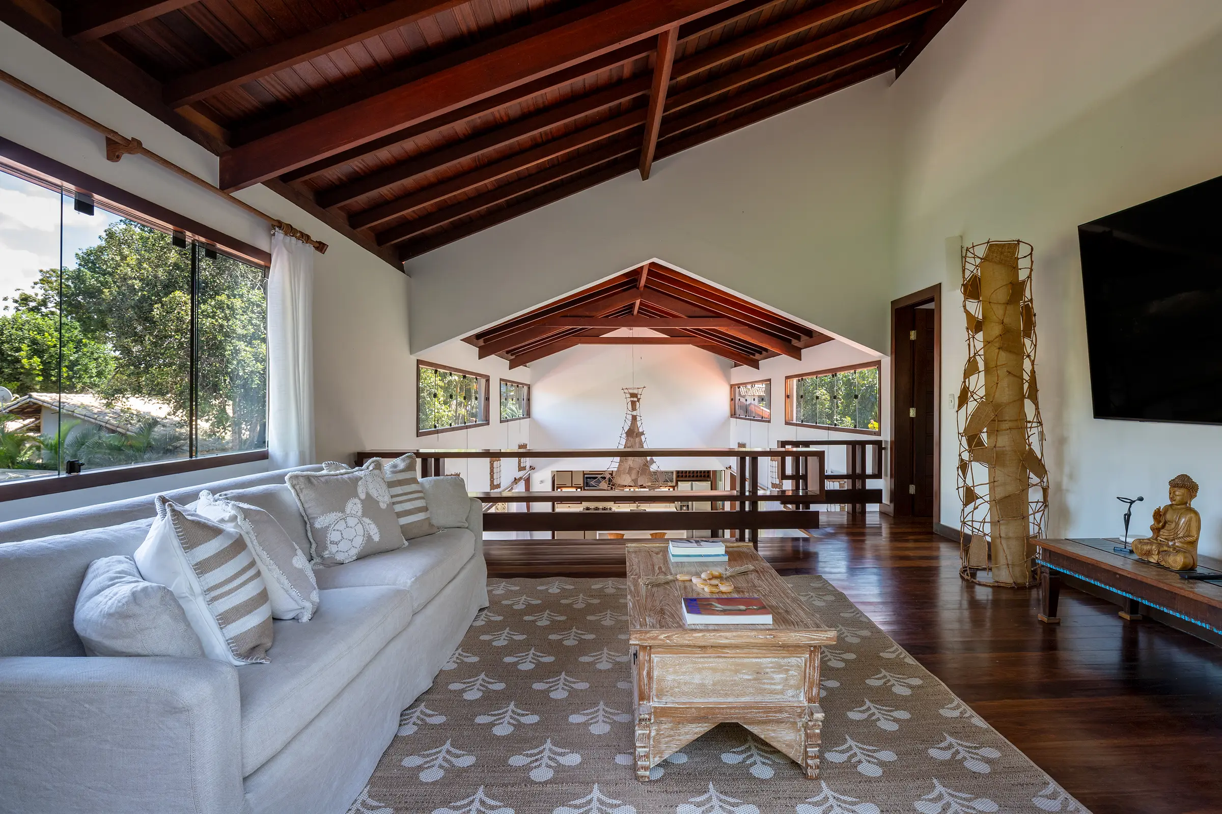 Sala com teto de madeira aparente, sofá branco e esculturas