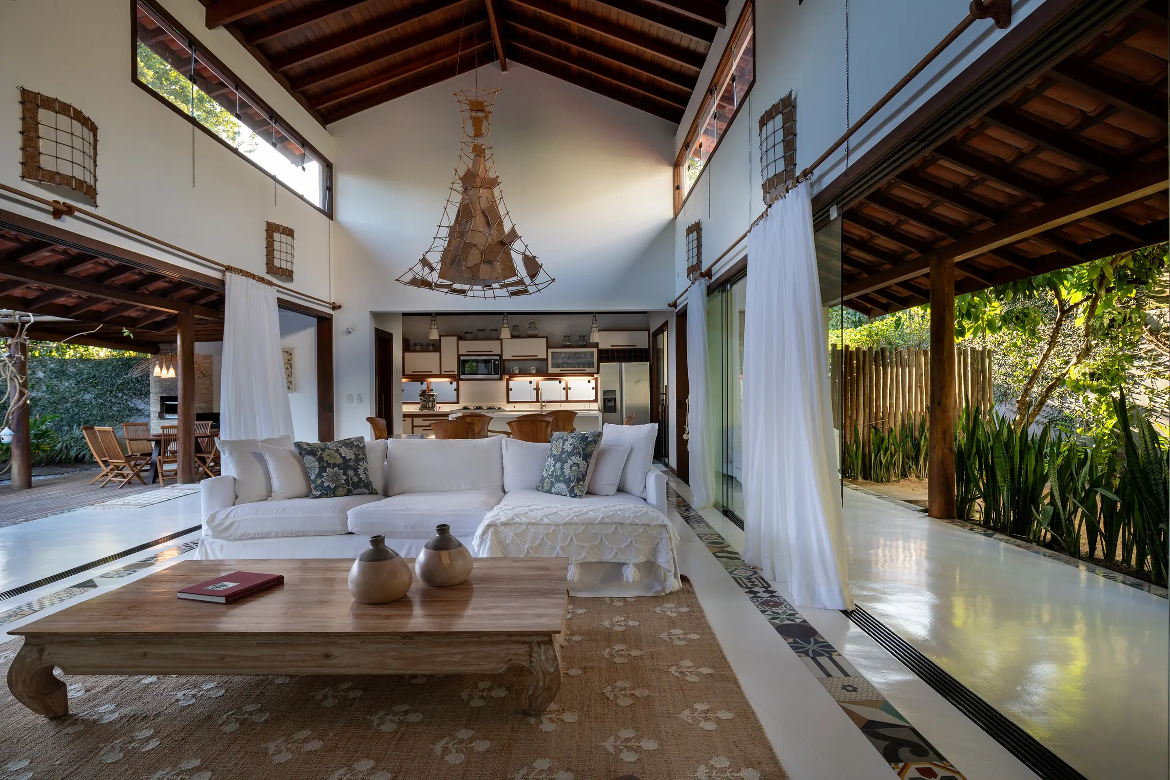 Sala de pé-direito alto com sofá branco e cozinha ao fundo