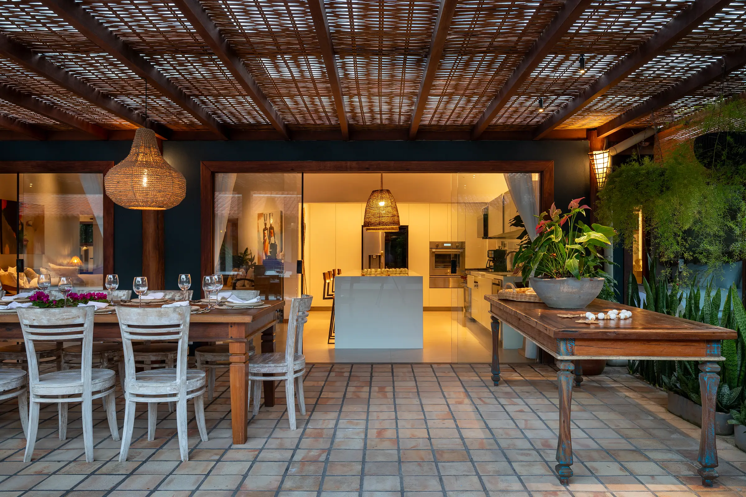 Terraço com mesa de jantar posta e a cozinha iluminada ao fundo