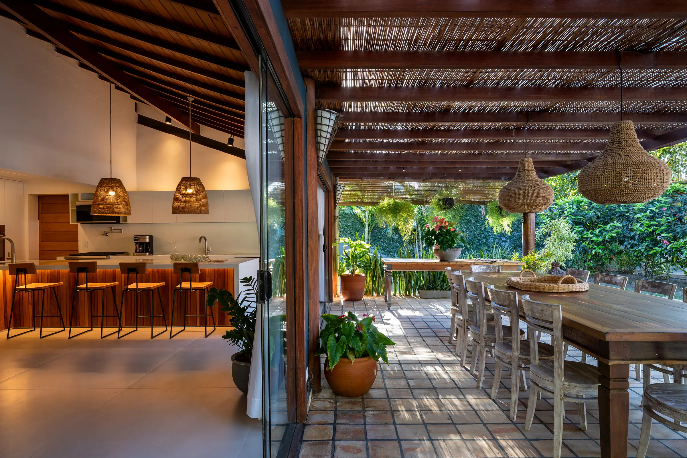 Cozinha aberta para o terraço com bancada, banquetas e luminárias de palha