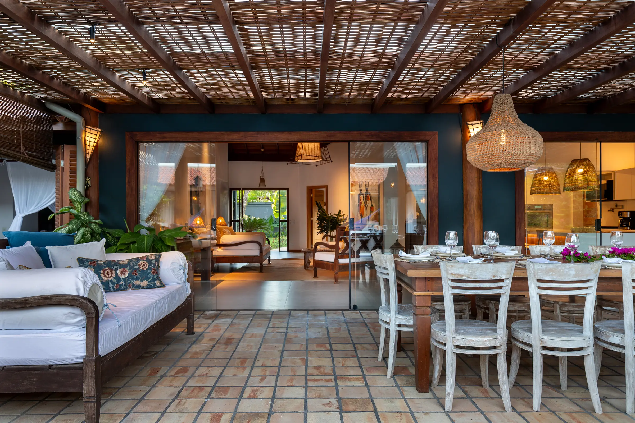 Terraço coberto com sofá, mesa de jantar posta e cozinha ao fundo