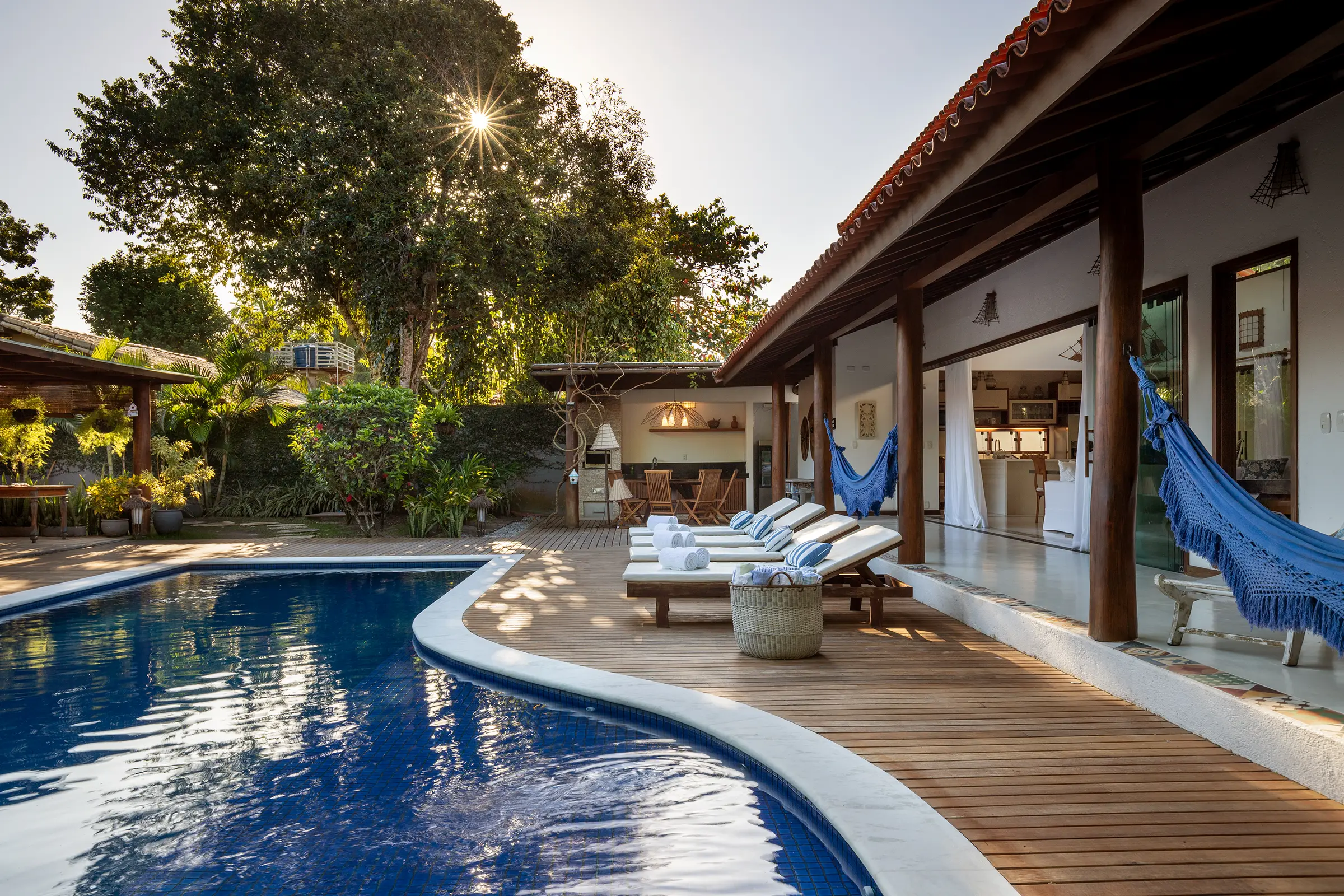 Deck de madeira contornando a piscina, com espreguiçadeiras e rede azul