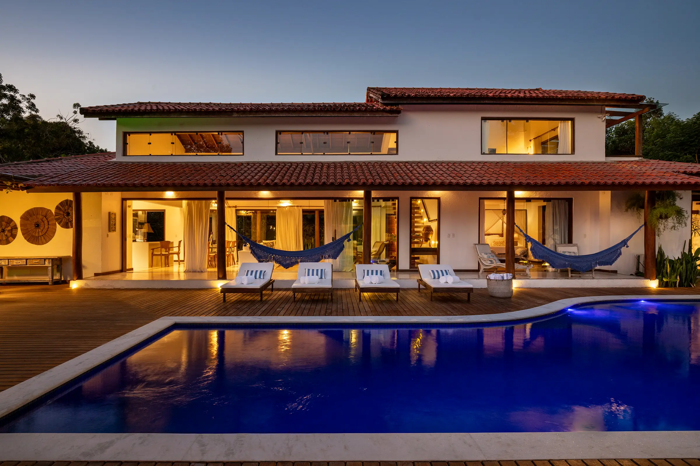 A casa ao entardecer, janelas acesas e piscina iluminada