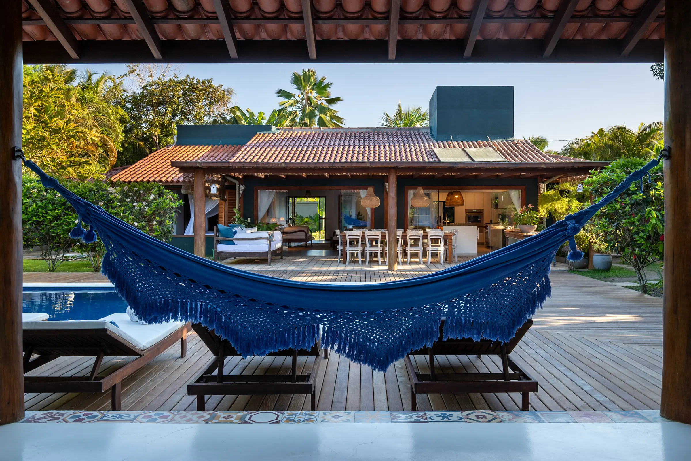 Rede azul com franjas diante da piscina e da casa de telhas
