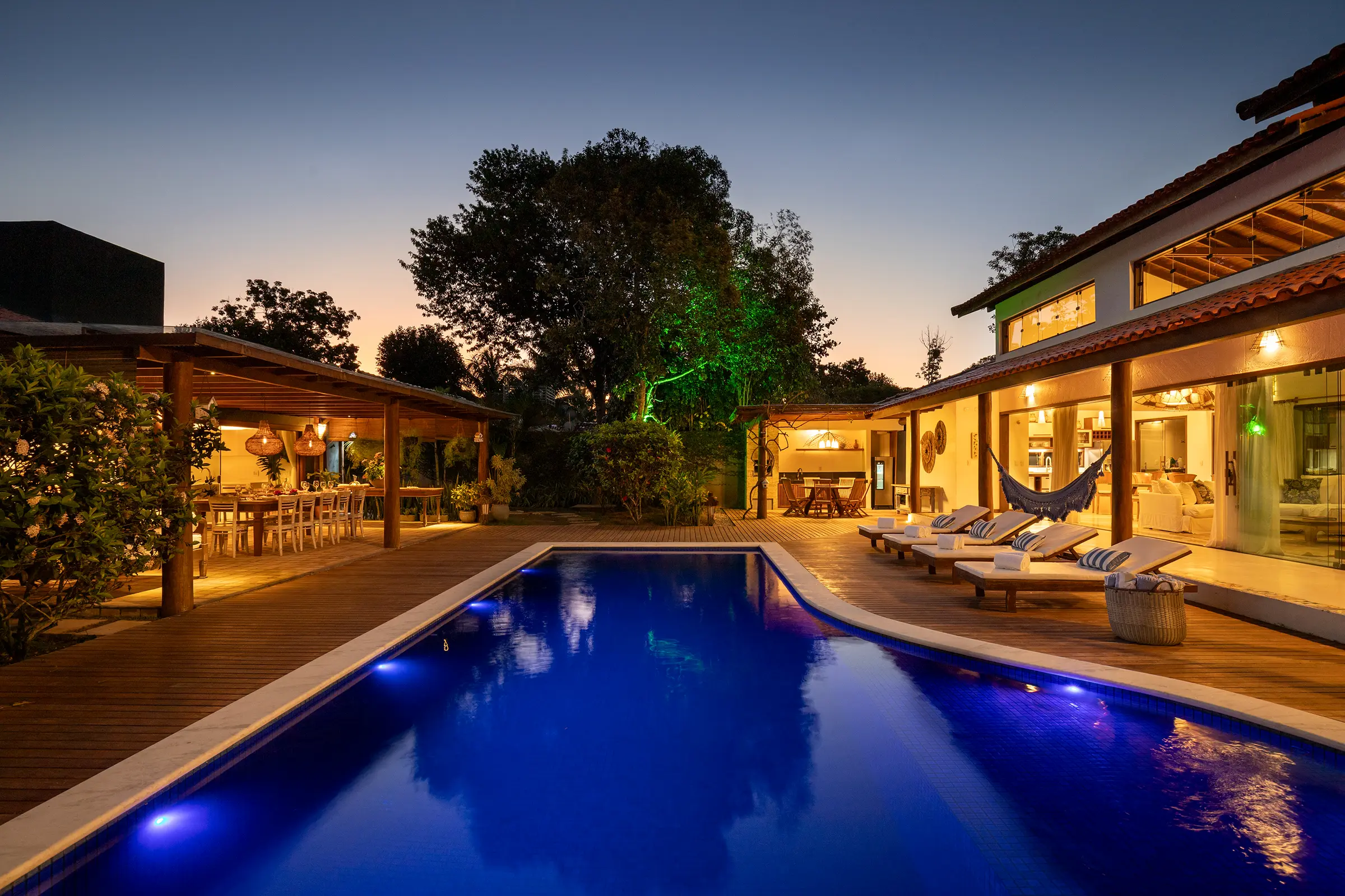 Piscina iluminada ao anoitecer, com a varanda e a área gourmet ao fundo