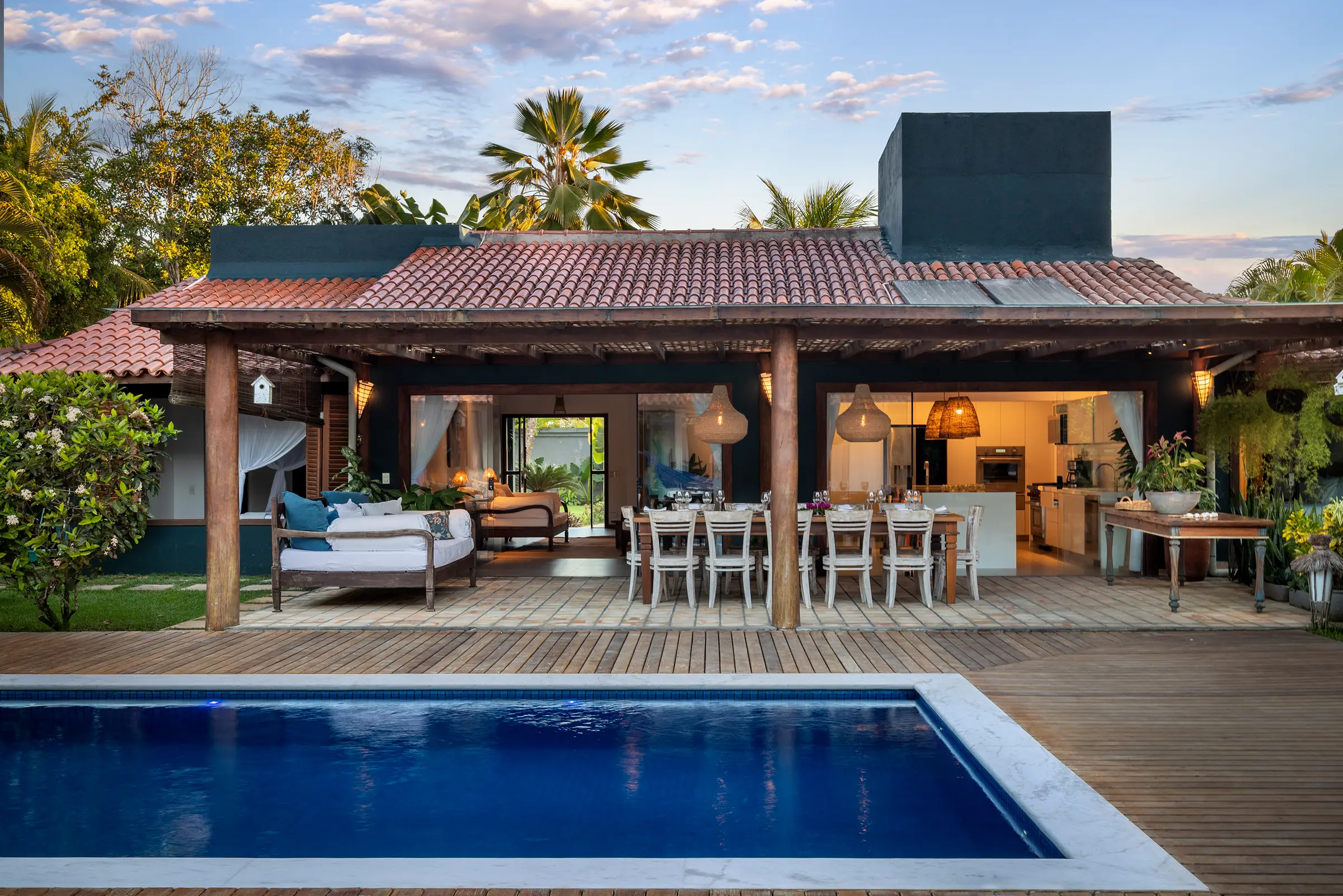 Pavilhão de madeira com mesa posta e piscina à frente, ao fim do dia