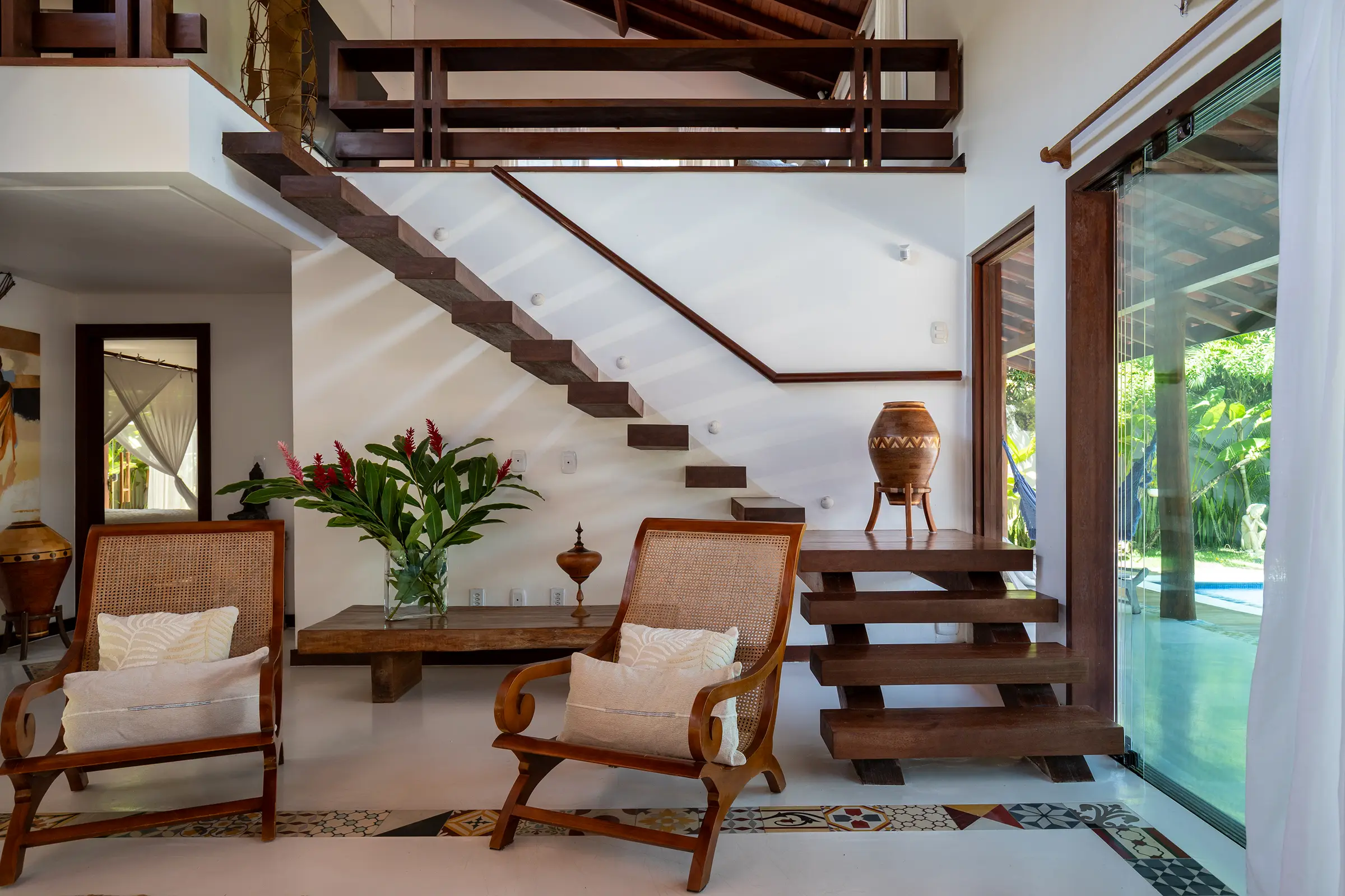 Escada de madeira, poltronas de palhinha e vaso com flores tropicais